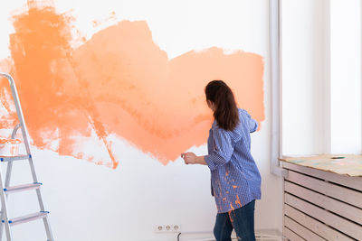 Young woman painting wall at home