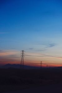 Silhouette electricity pylons on landscape against blue sky