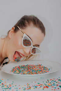 Close-up of woman wearing sunglasses with confetti against gray background