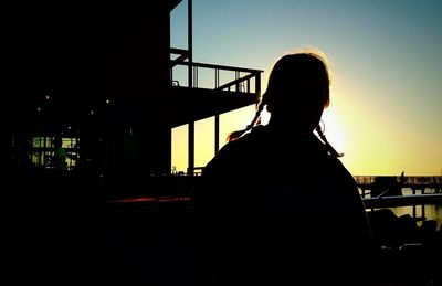 Woman standing by railing at sunset