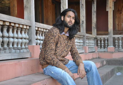 Side view of a charming long haired young man looking at camera while sitting in old temple stairs