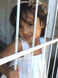 Portrait of cute girl standing looking through metal gate