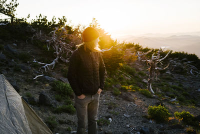 Woman looking away while standing by tent against sky during sunset