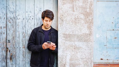 Full length of a young man  with a phone against wall