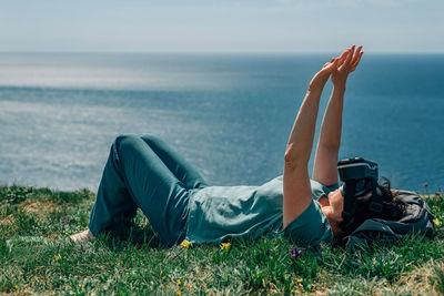 Adult woman lies mountain against the background  sea in summer, spring in virtual reality glasses. 