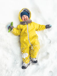 Smiling toddler in bright yellow jumpsuit on snow. laughing child walking outdoors in snowy weather. 