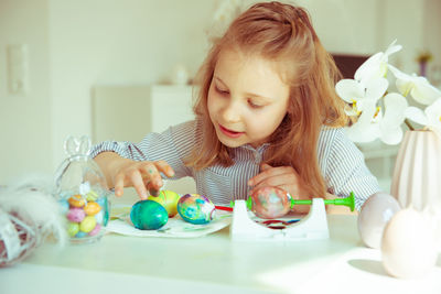 Cute girl painting easter egg while sitting at home