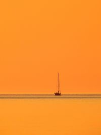 Sailboat sailing on sea against clear sky during sunset