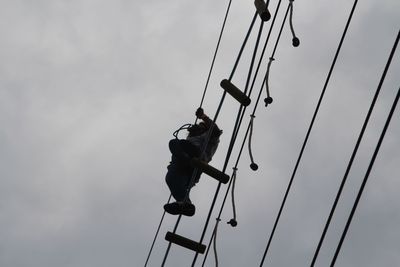 Low angle view of man working on rope against sky