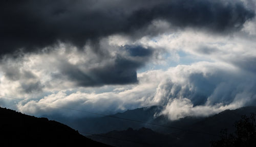 Low angle view of storm clouds over silhouette mountain
