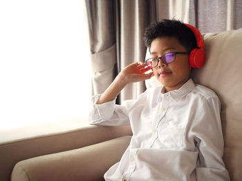 Boy with eyes closed listening music while sitting on sofa at home