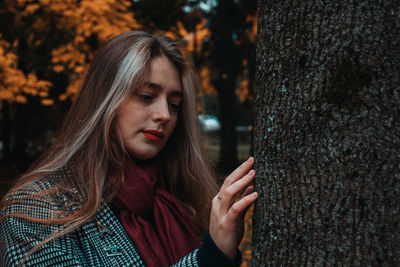 Thoughtful young woman touching tree trunk while standing in park