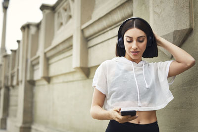 Woman with headphones using smart phone by wall in city