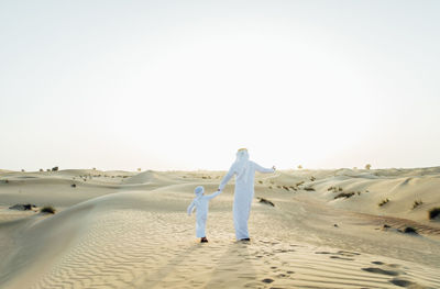 Rear view of people walking on beach against clear sky