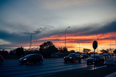 Cars on street against sky at sunset