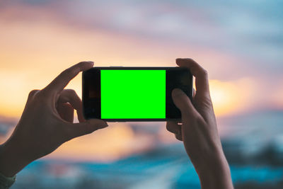 Close-up of hand holding camera against sky during sunset