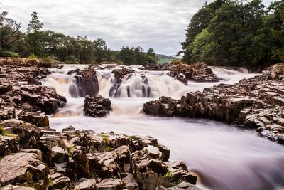 Idyllic view of waterfall in forest against sky