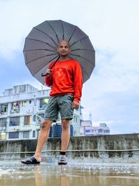 Full length of man standing on wet umbrella during rainy season