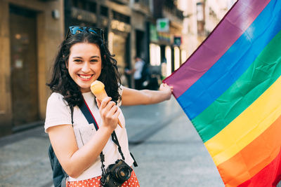 Portrait of smiling woman holding ice cream and flag standing outdoors