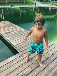 High angle view of shirtless boy standing on jetty over lake