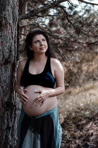 Smiling pregnant woman standing by tree at forest