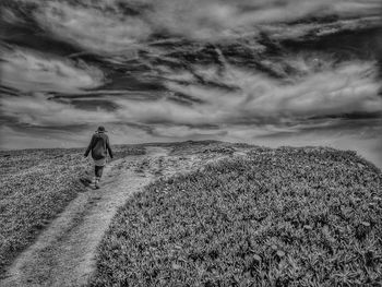 Rear view of man walking on land against sky