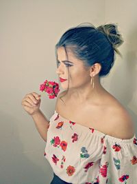 Close-up of beautiful young woman with flower standing against wall