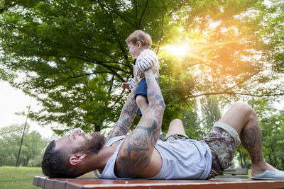 Father carrying son while lying on table against trees