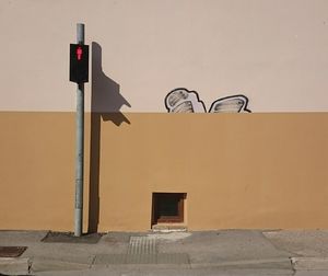 Illuminated road signal on footpath against wall