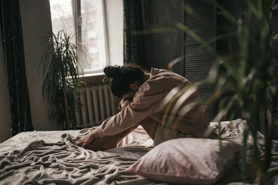 Side view of young man sitting on bed at home