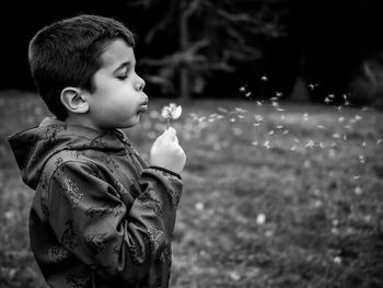 Side view of boy blowing dandelion while standing on grass 