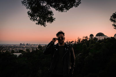 Portrait of man standing by tree against sky during sunset