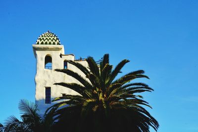 Low angle view of palm tree and heritage building against blue sky