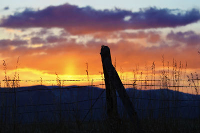 Silhouette fence on field against sky during sunset