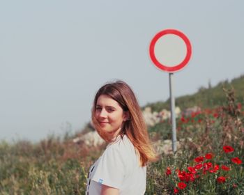 Portrait of smiling young woman standing by plants against sky