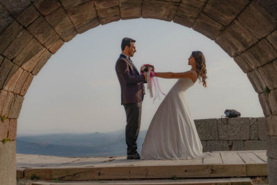 Side view of bride and groom posing seen through stone arch