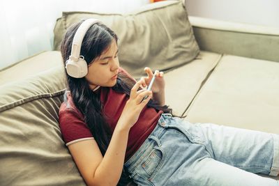 Young woman using phone while sitting on sofa at home