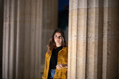 Portrait of woman standing against pillar at night