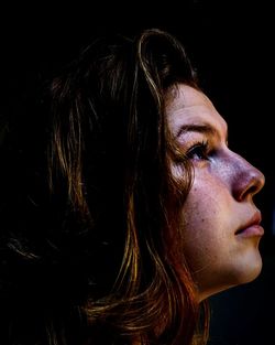 Close-up of young woman against black background