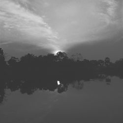 Silhouette trees by lake against sky
