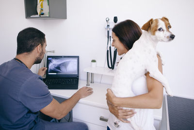 Woman carrying dog talking with veterinarian in hospital