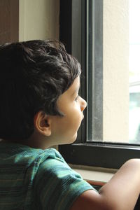 Curious boy looking through window while sitting at home