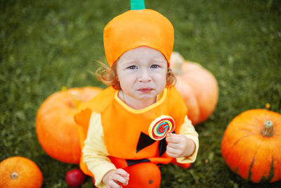 High angel view of cute girl wearing costume sitting by pumpkin at park