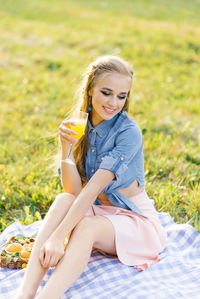 Pretty caucasian young woman with long hair is sitting on a blanket in nature on a sunny summer day
