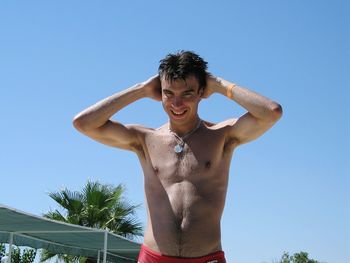 Low angle view of shirtless young man standing against clear blue sky