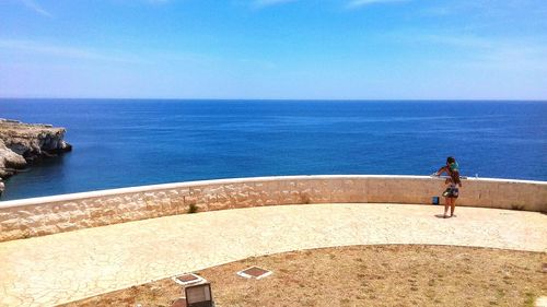 Man standing on retaining wall by sea against clear sky