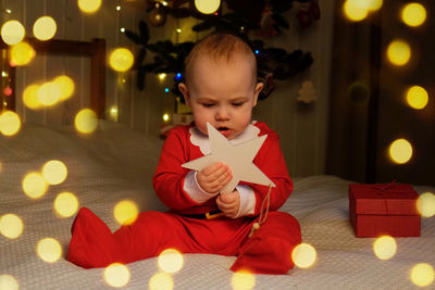 Christmas baby in red santa costume playing on white soft bed. smiling 7 month newborn baby in santa