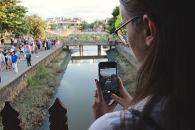 Close-up of woman photographing canal with mobile phone in city