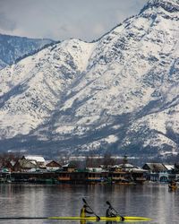 Male friends rowing boat in lake against snowcapped mountains