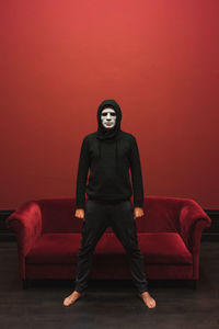 Full length of man wearing mask standing against red wall